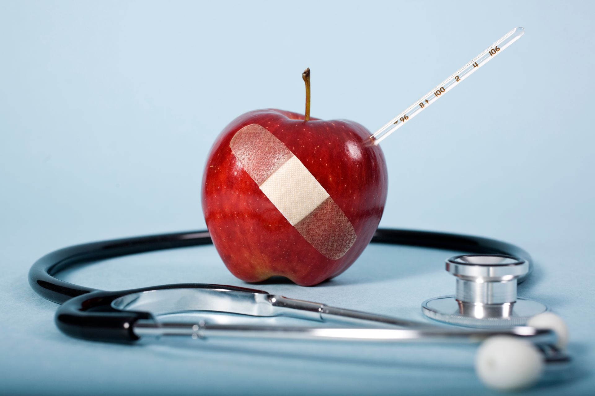 An apple with a bandage on it next to a stethoscope and a thermometer