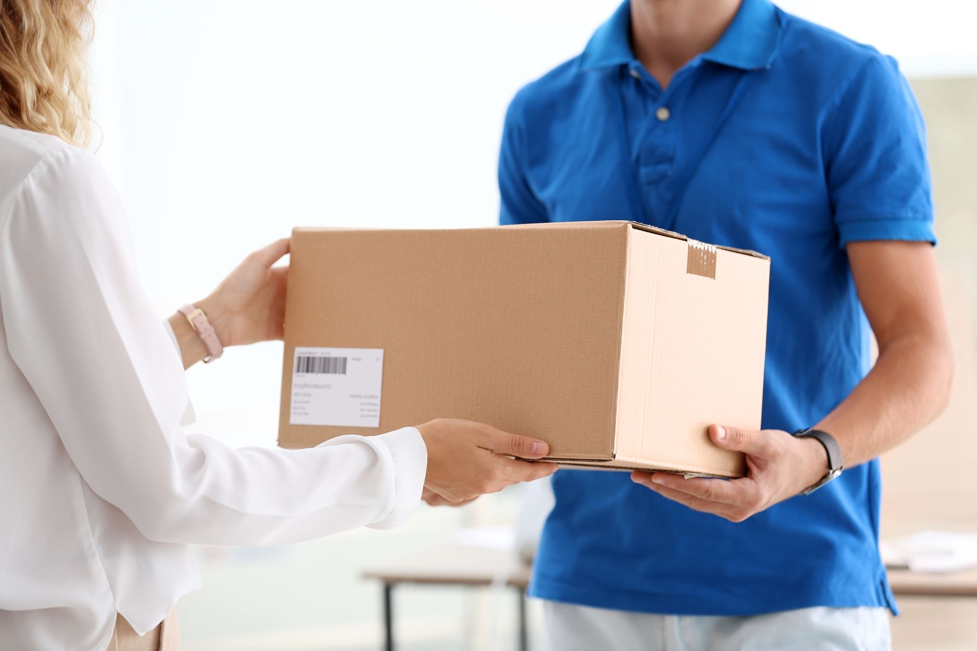 A woman is handing a box to a delivery man.