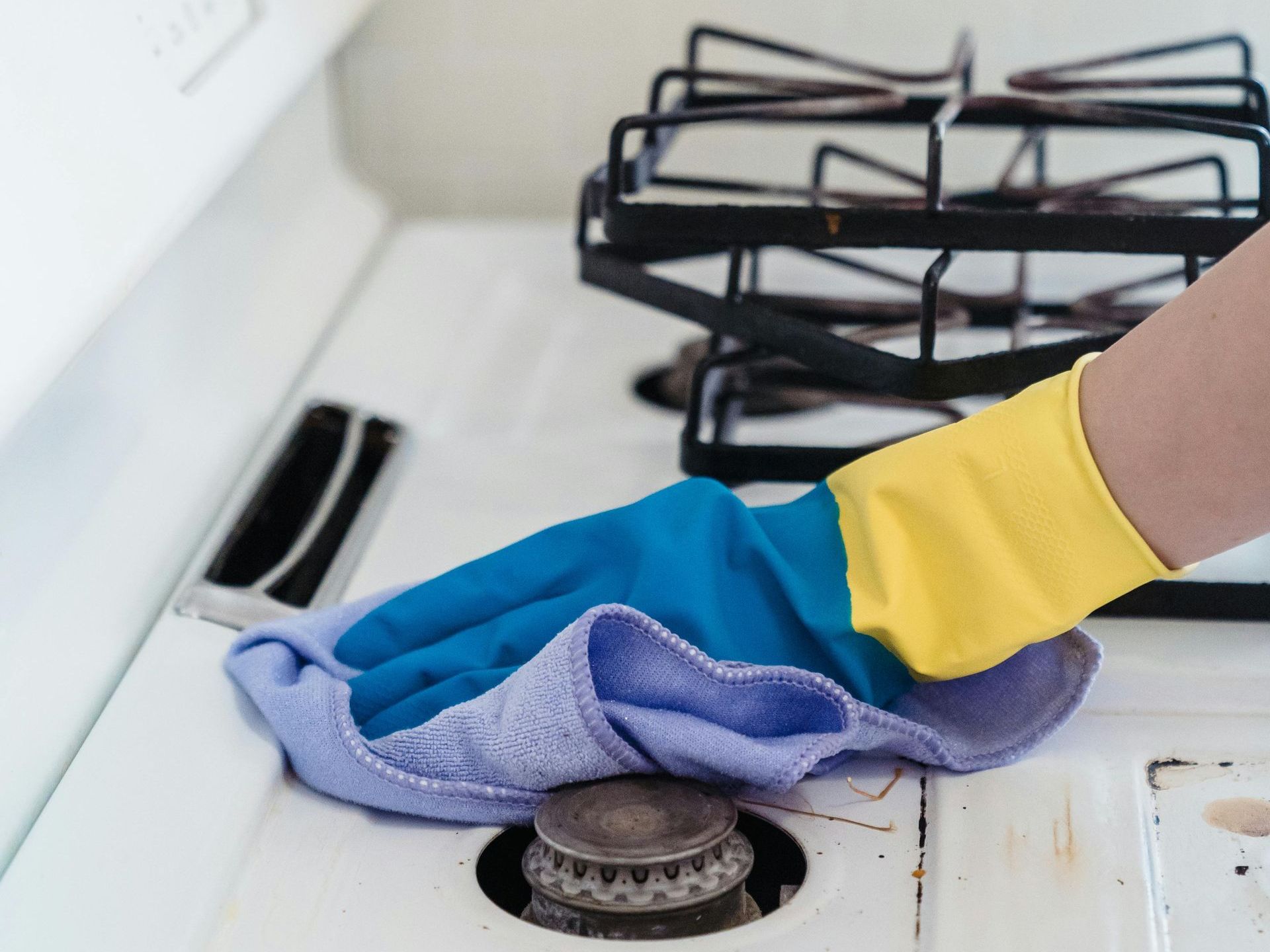 A person wearing rubber gloves is cleaning a stove with a cloth.