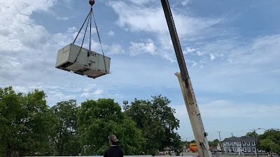 A man is standing next to a crane lifting a large box.