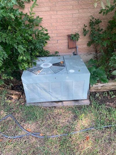 An air conditioner is sitting in the grass next to a brick wall.