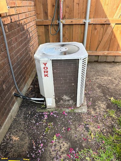 A york air conditioner is sitting on the side of a brick building next to a wooden fence.