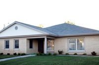 A small house with a gray roof and a white trim is sitting on top of a lush green lawn.