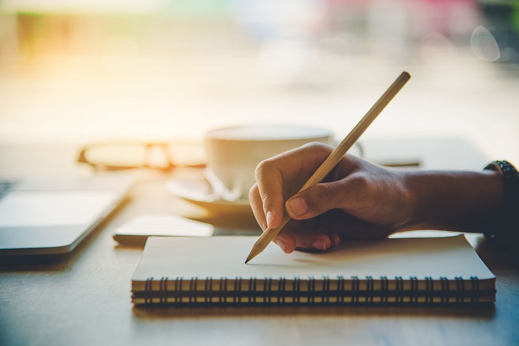 A person is writing in a notebook with a pencil.
