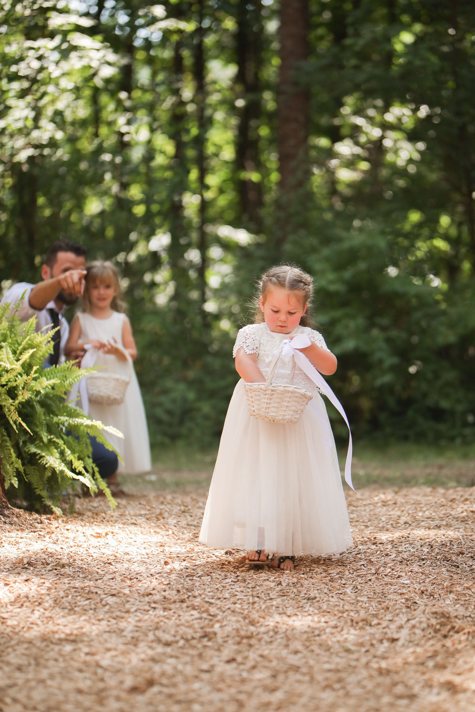 A flower girl in a white dress is holding a basket of flowers.