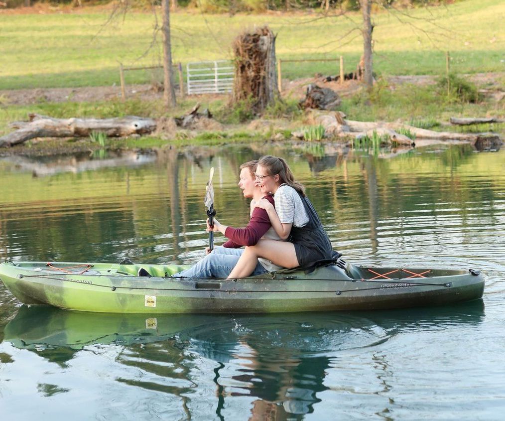 A couple is sitting on top of a kayak in the water.