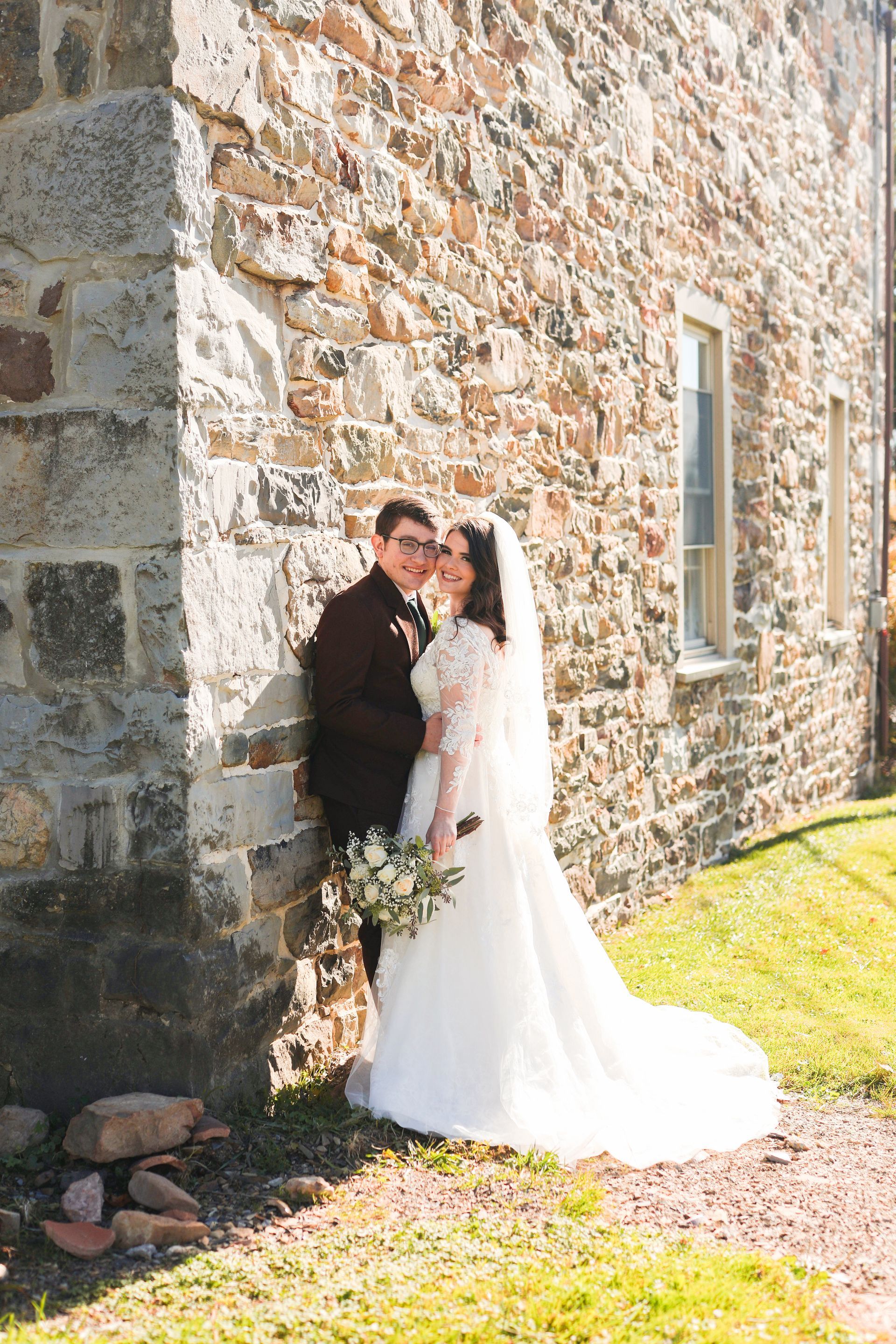 A bride and groom are posing for a picture in front of a stone wall.