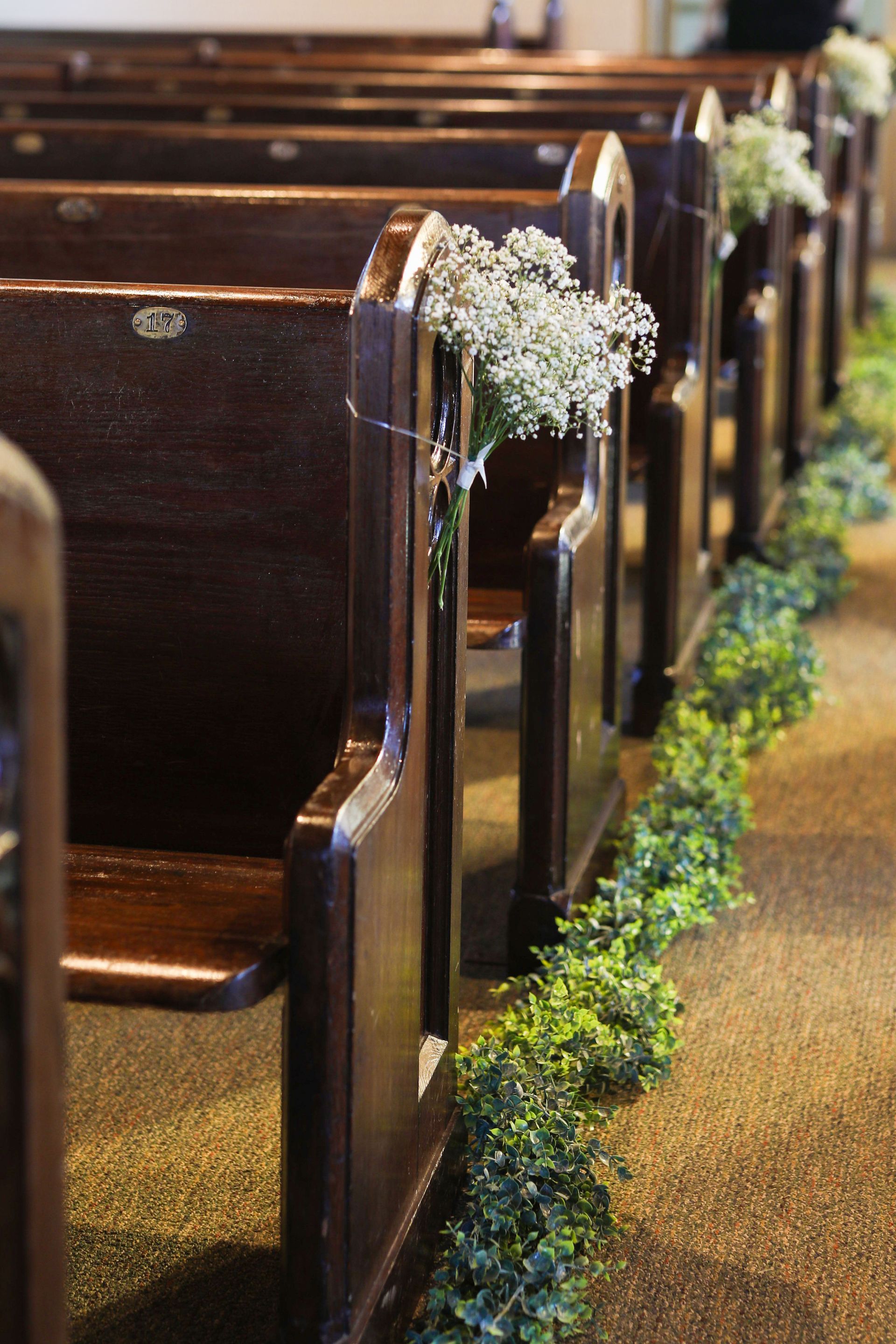 A row of wooden benches in a church decorated with baby 's breath and greenery.
