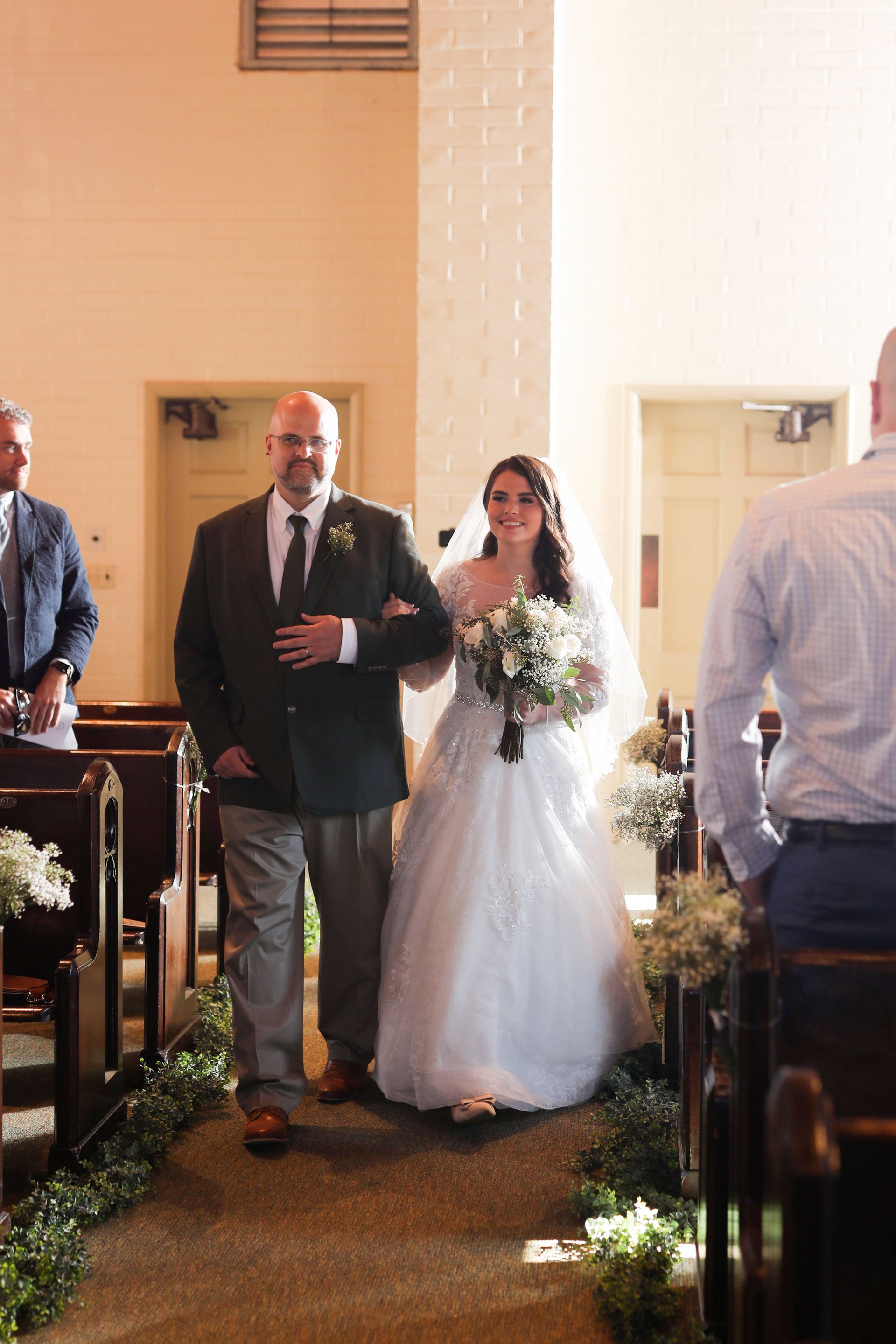A bride and her father are walking down the aisle of a church.