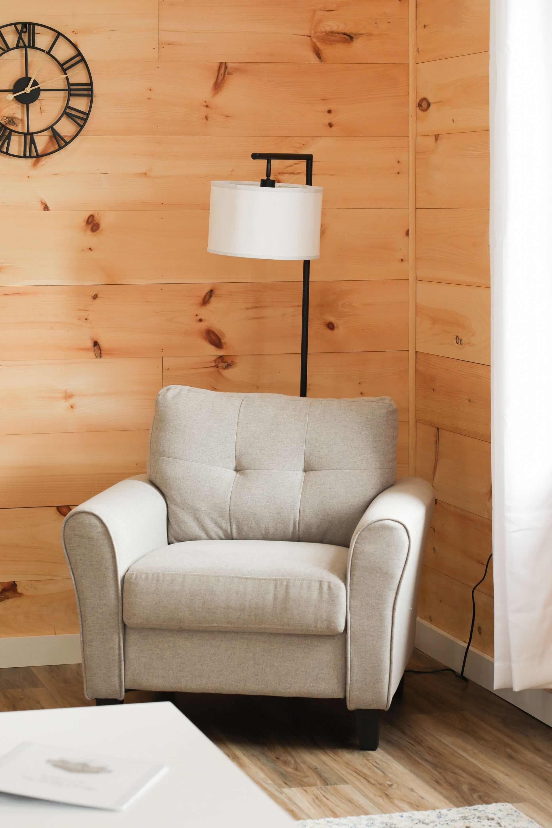 A living room with a chair a lamp and a clock on the wall
