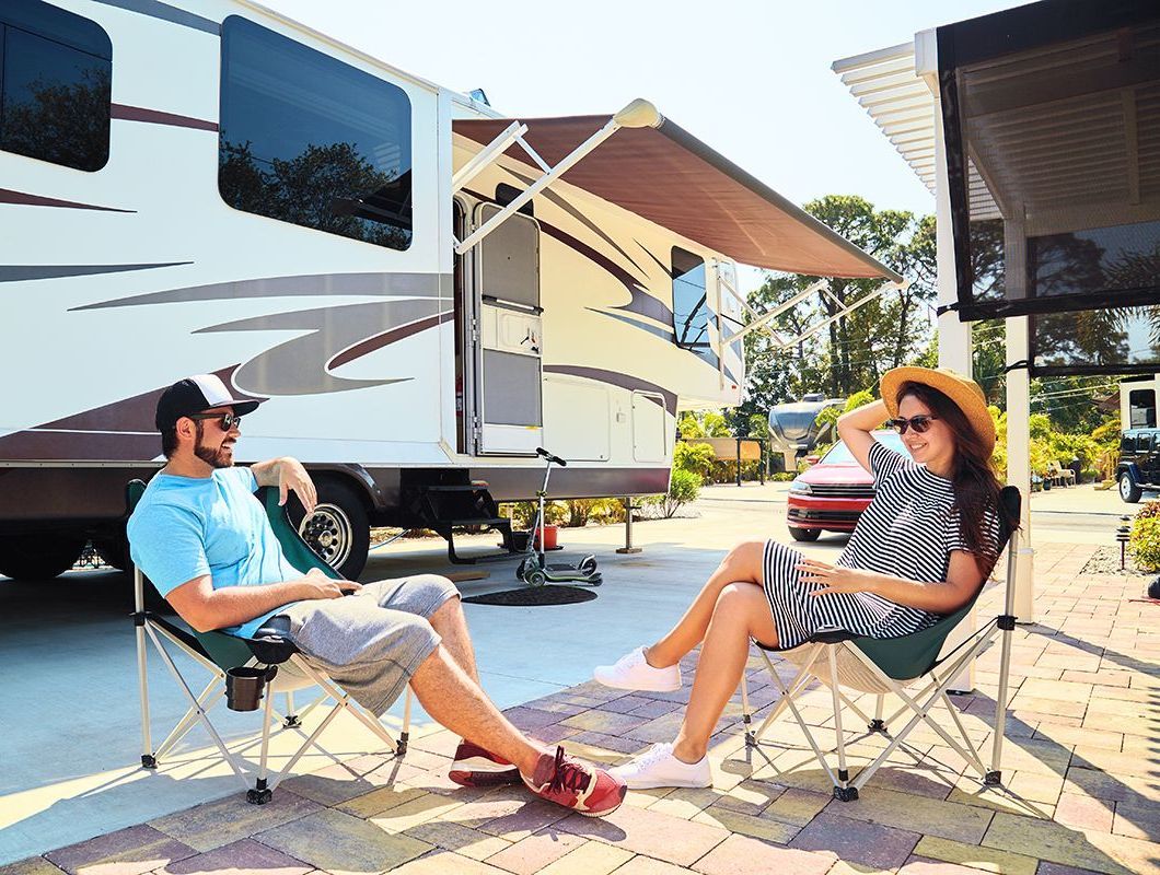 A man and a woman are sitting in chairs in front of a rv.