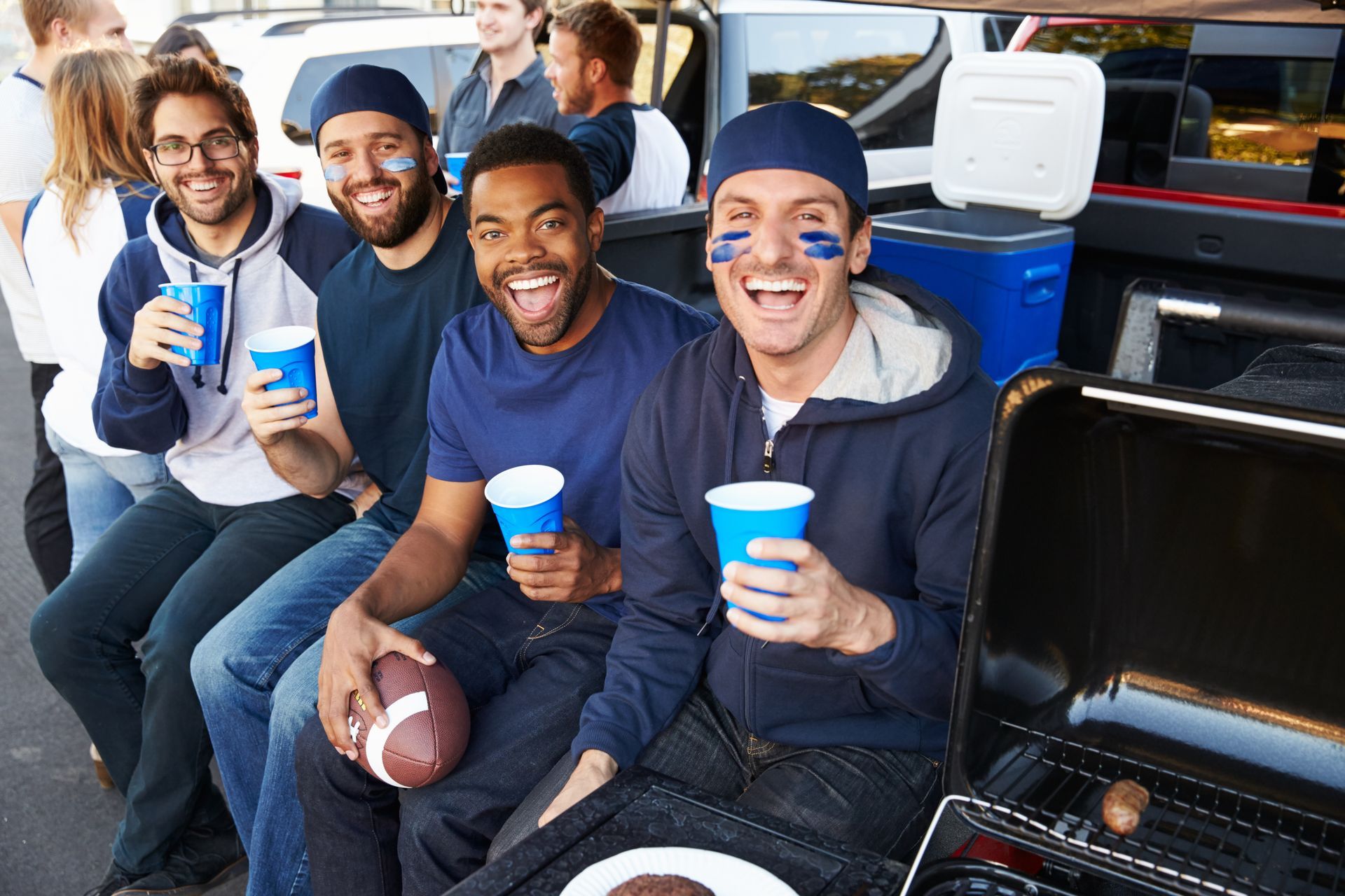 A group of men are sitting in the back of a truck holding cups and a football.