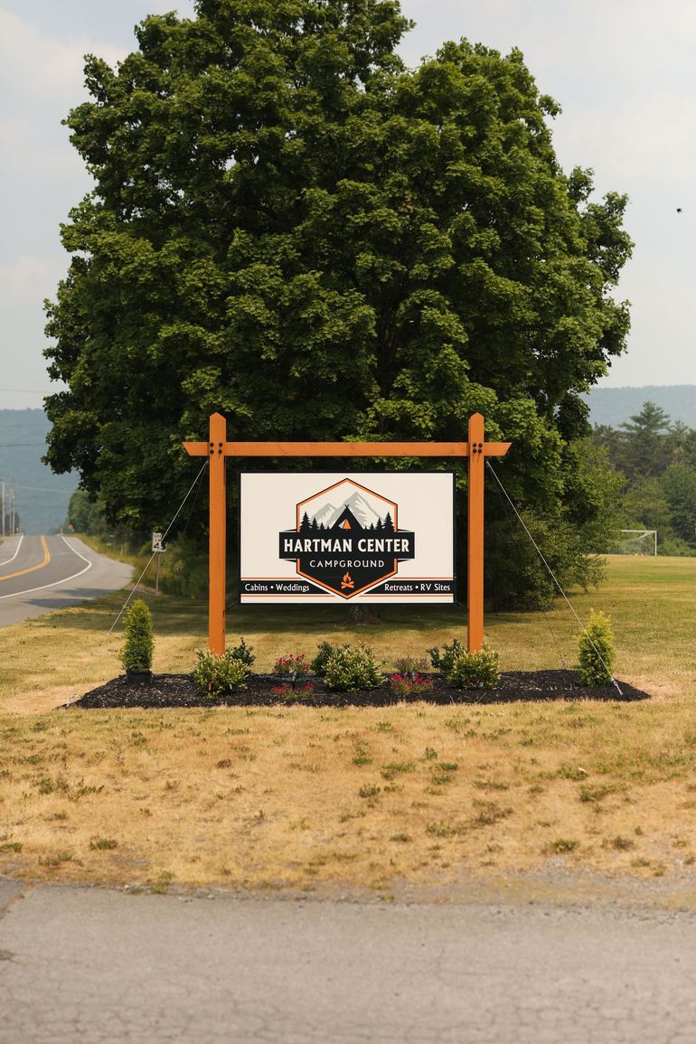 A sign in a field with a tree in the background.
