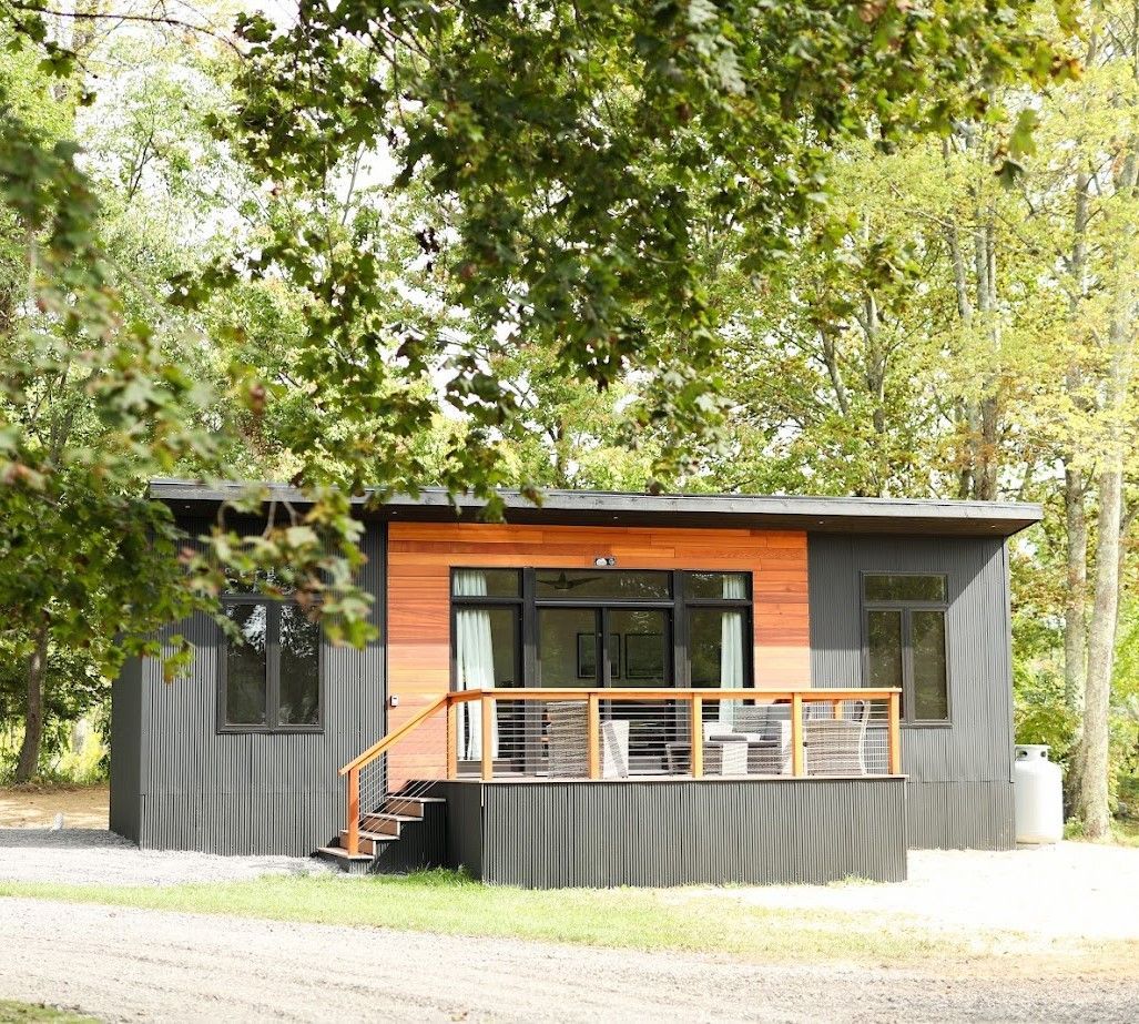 A small house with a porch and stairs is surrounded by trees.