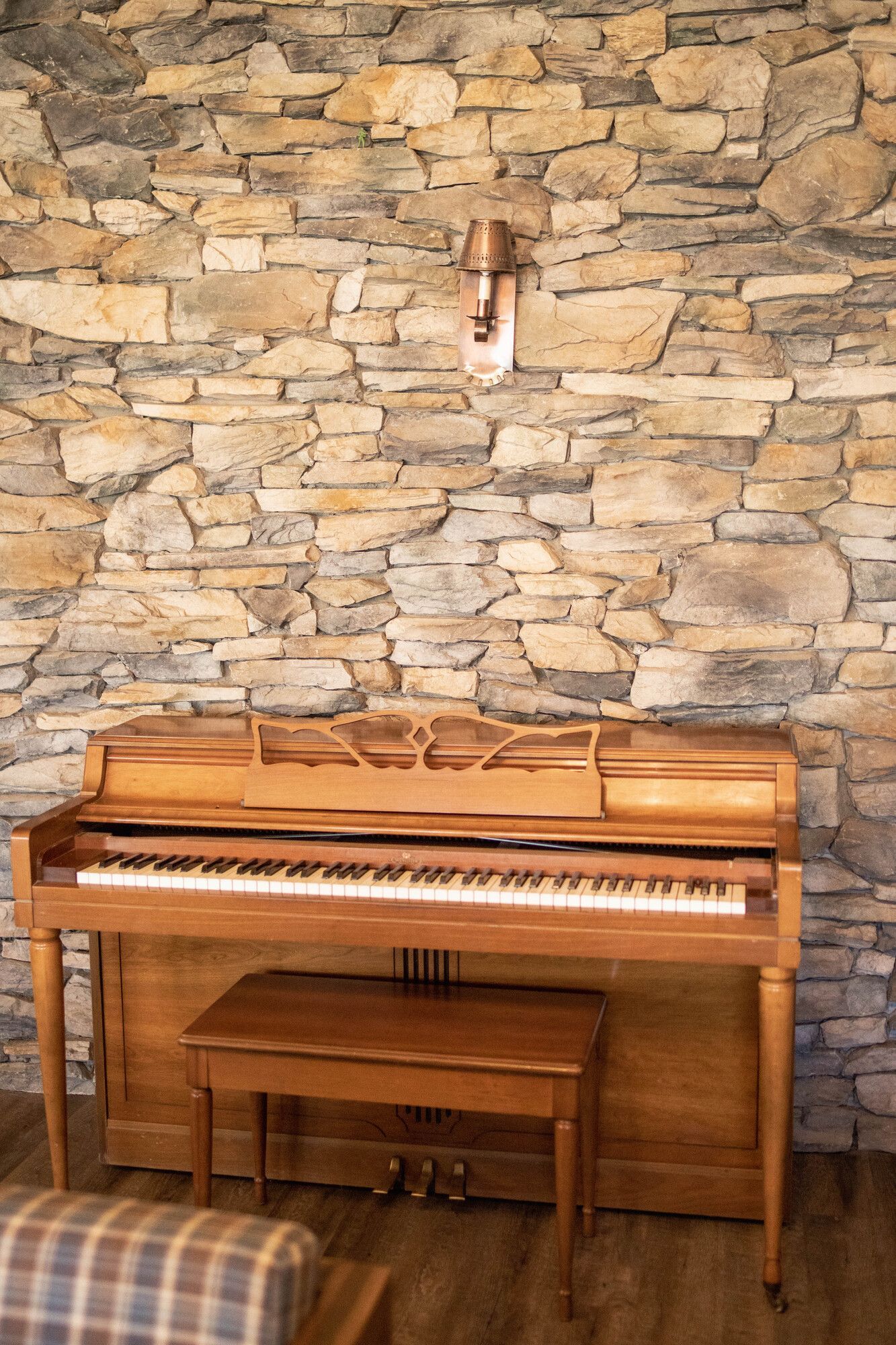 A piano is sitting in front of a stone wall.