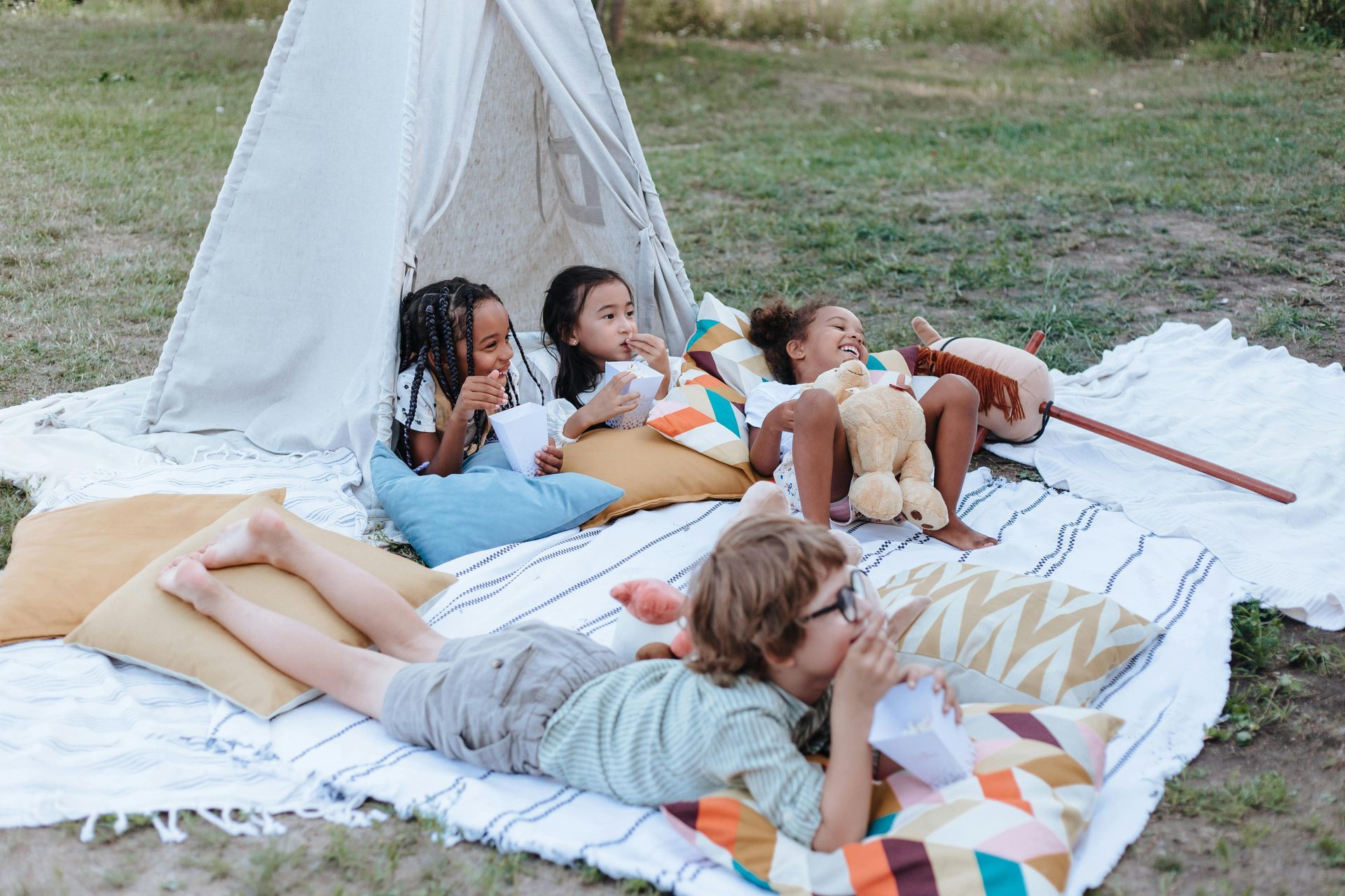 A group of children are laying on a blanket in front of a teepee.
