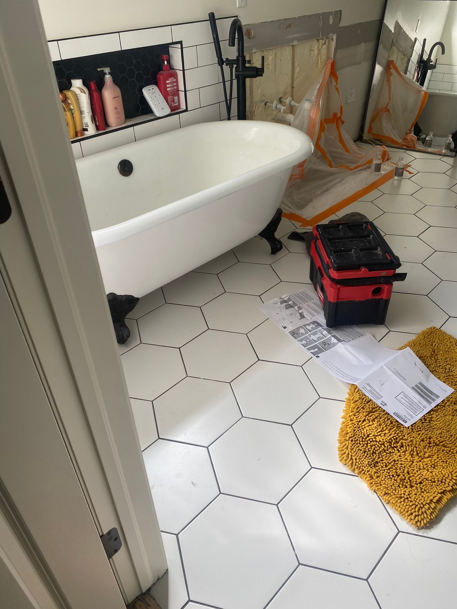 Bathroom with clawfoot tub, hexagonal white tile floor, and a black toolbox.