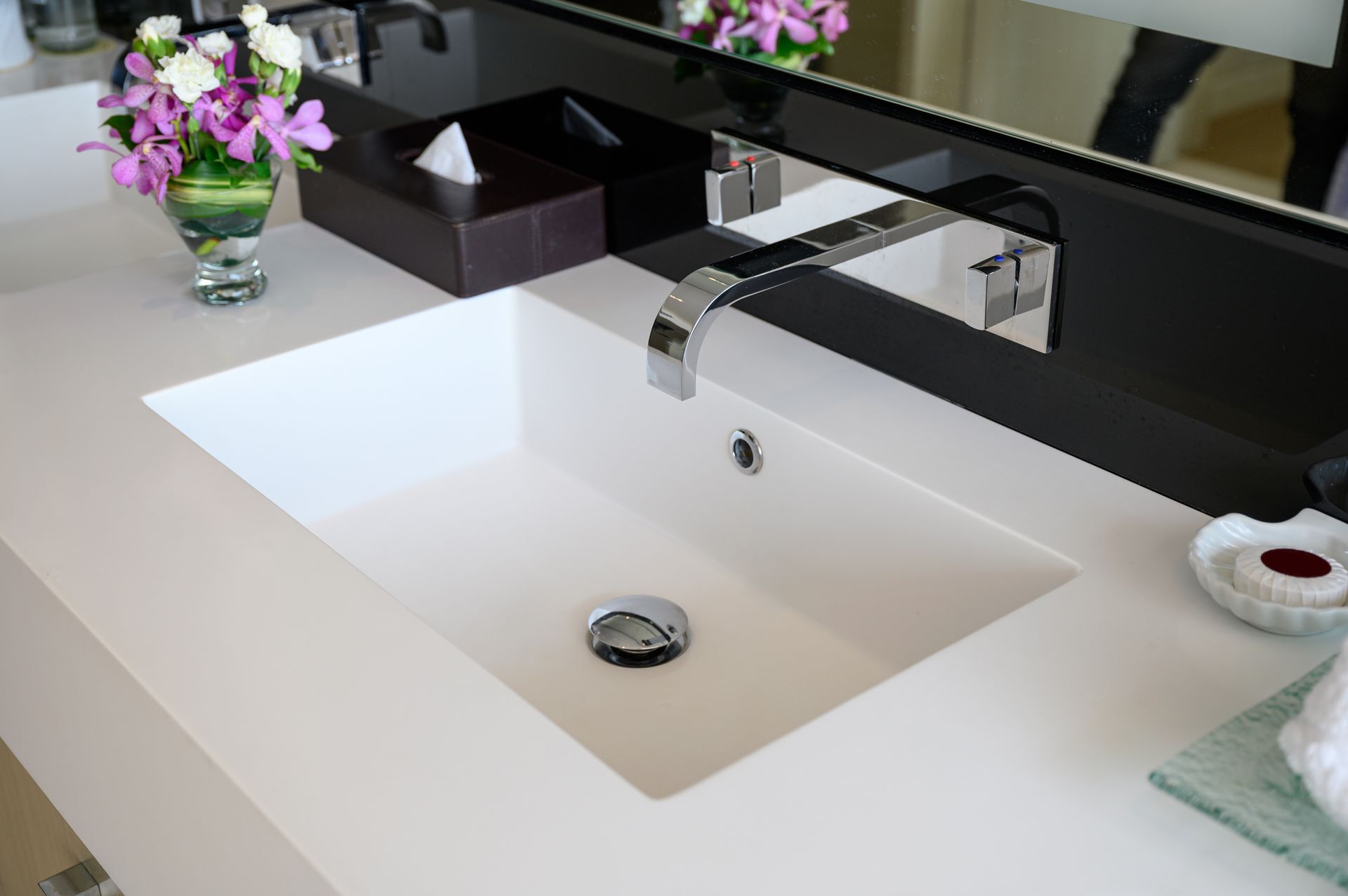 White rectangular bathroom sink with chrome faucet, flowers, and tissue box on countertop.