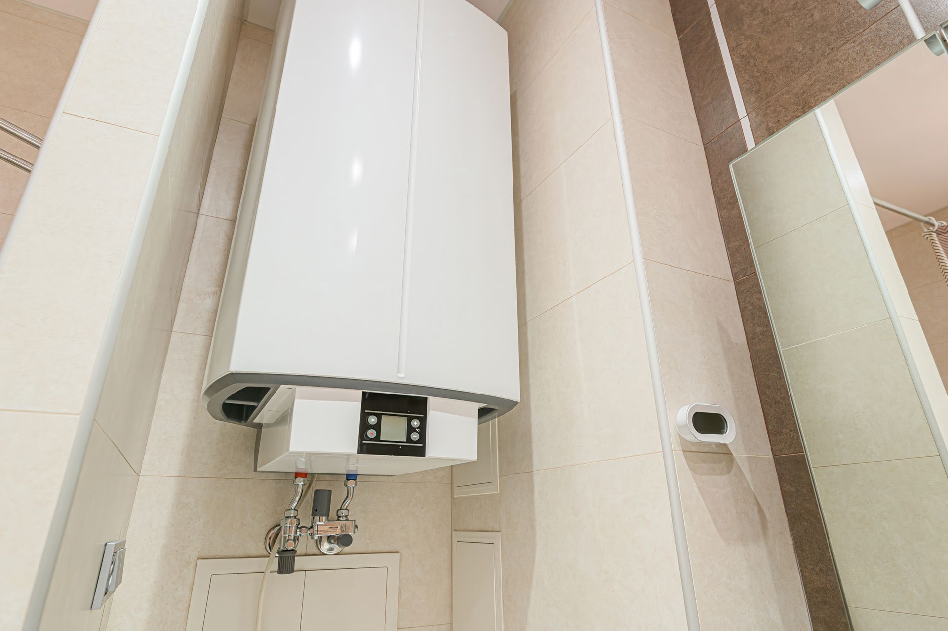 White water heater mounted on a tiled bathroom wall with pipes and a digital display.
