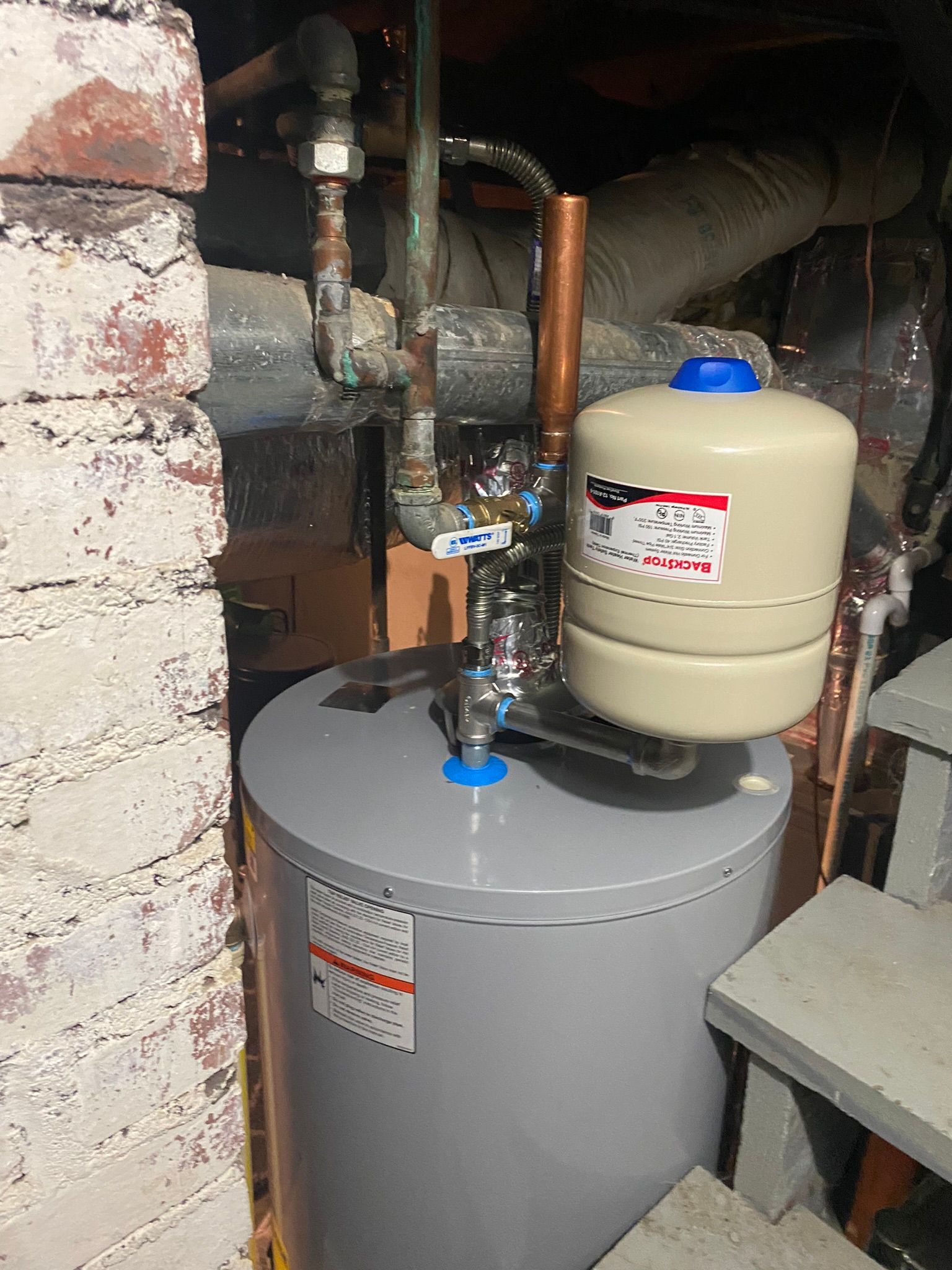Water heater with copper pipes, tank, and pressure relief valve in a basement setting.