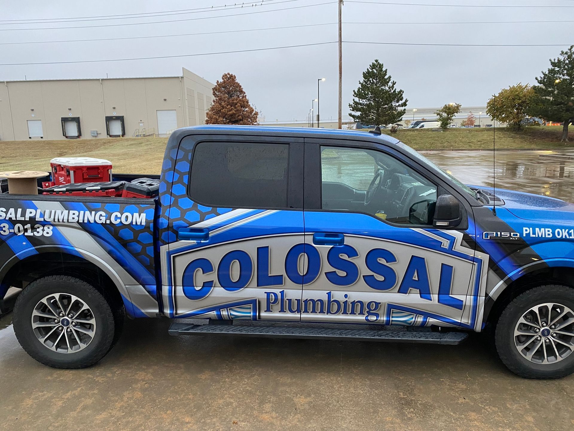Colossal Plumbing truck with blue and silver graphics parked outside, cloudy day.