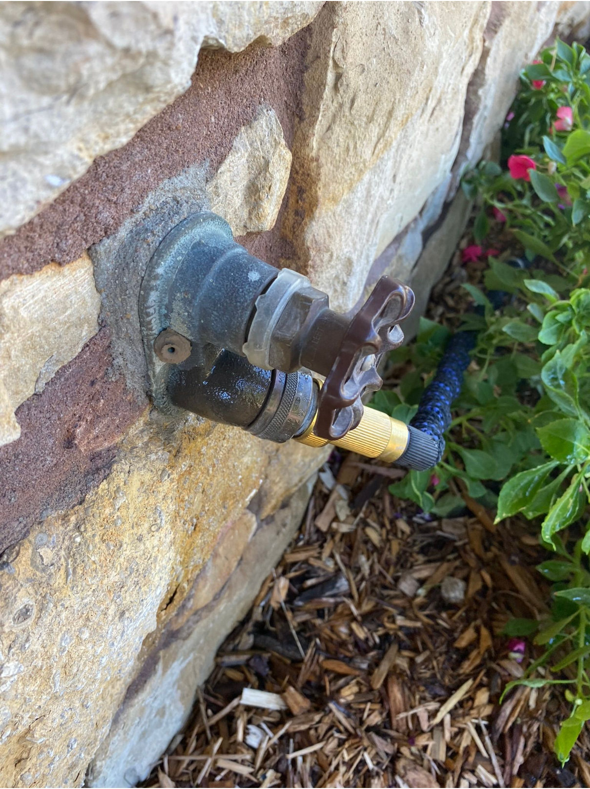 A hose is attached to a faucet on the side of a stone wall.