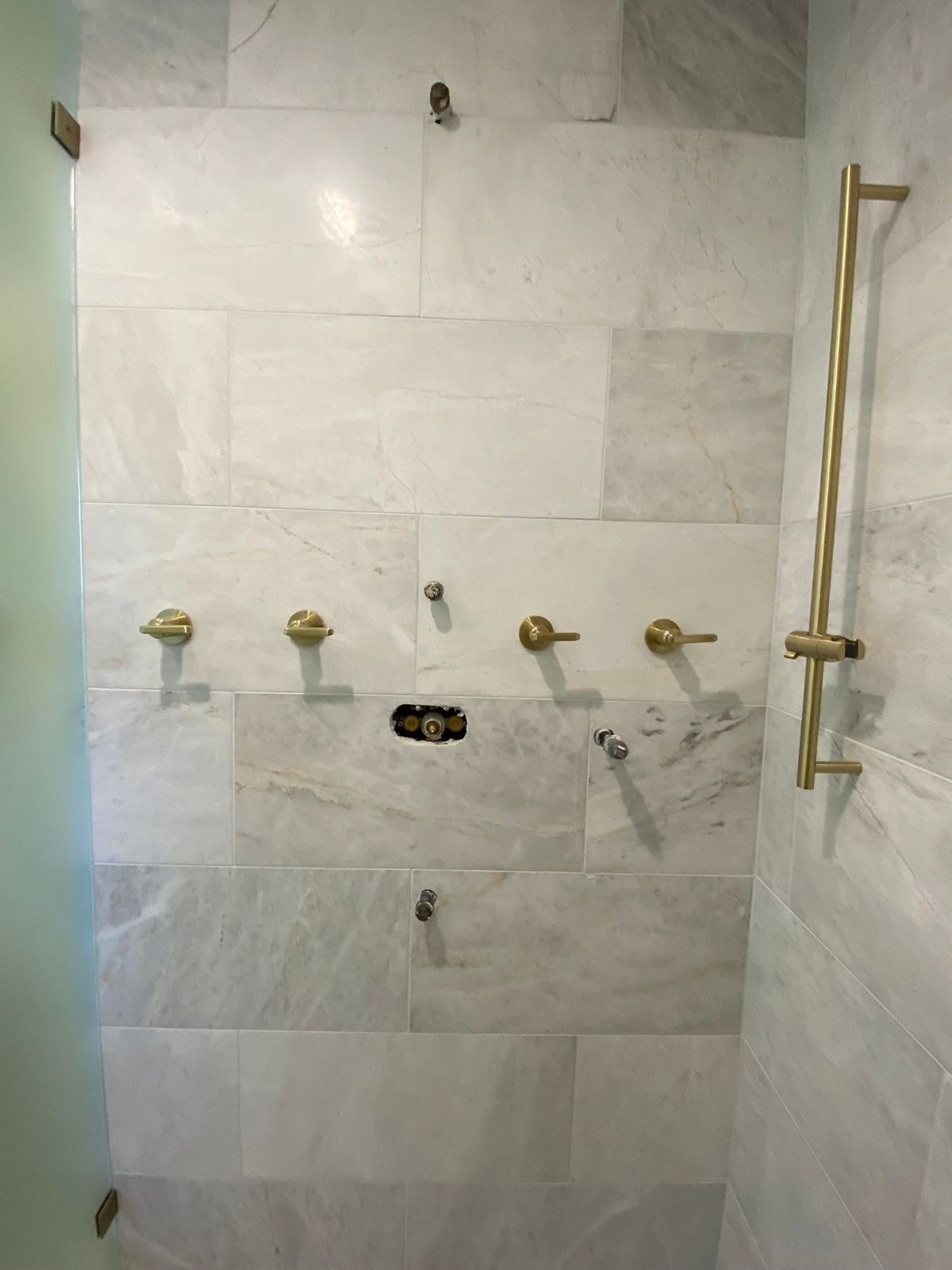 A shower with a marble wall and brass handles.