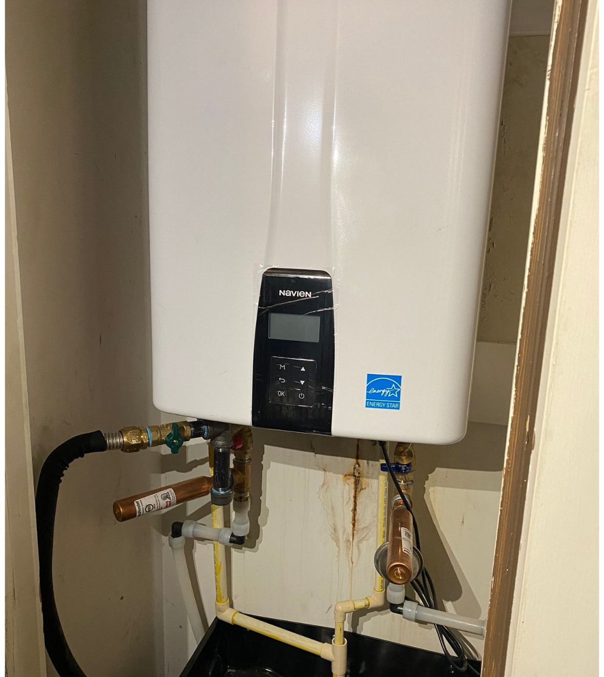 A white water heater is hanging on a wall next to a door.
