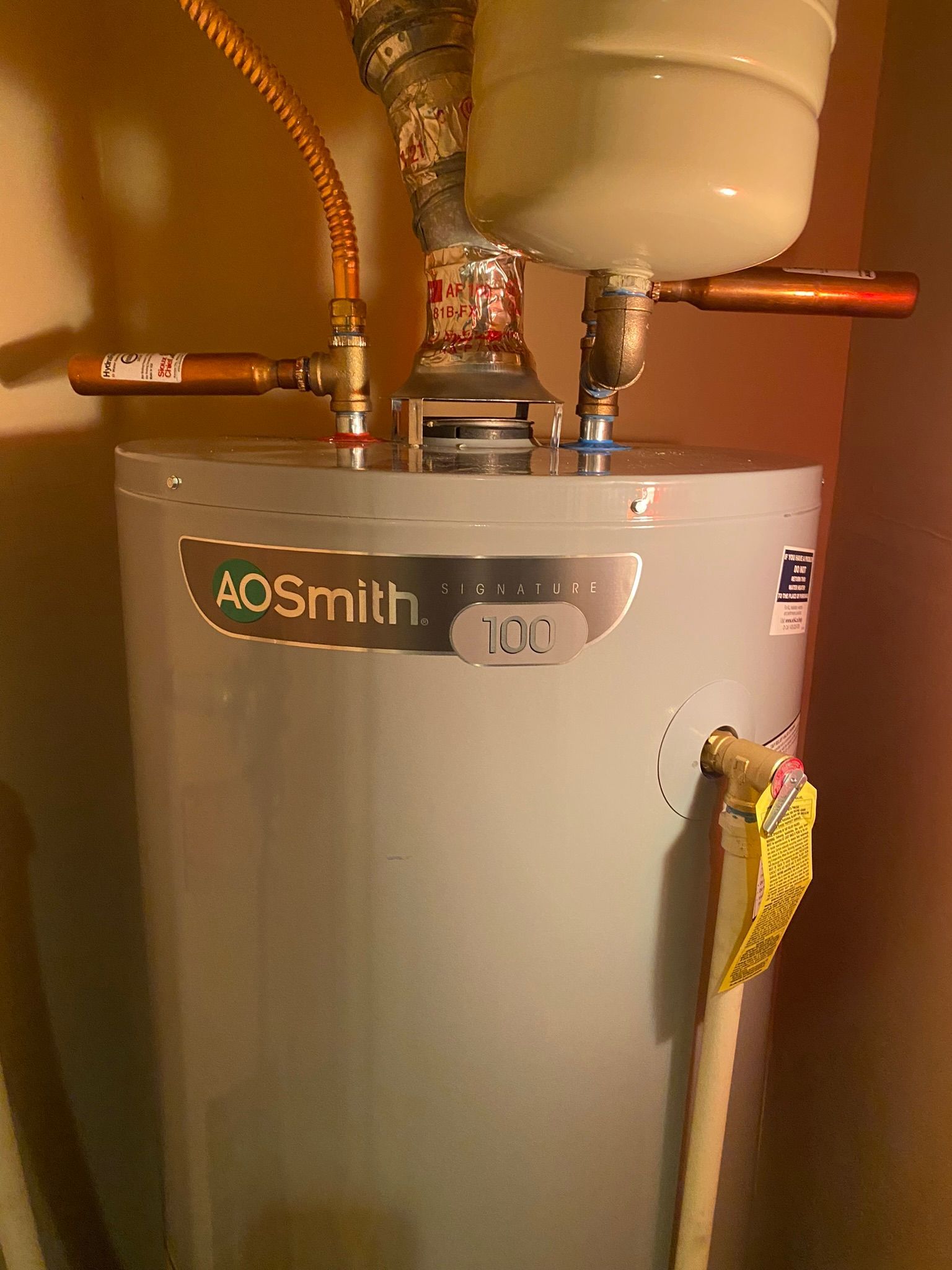 A white water heater is sitting in a room next to a wall.