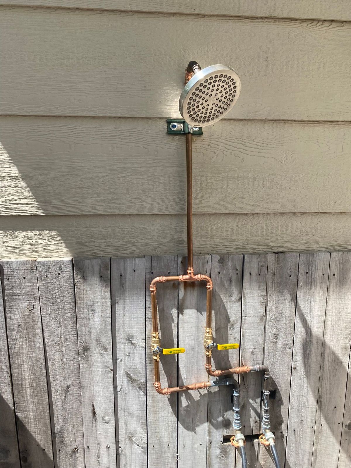 A shower head is attached to a wooden fence.