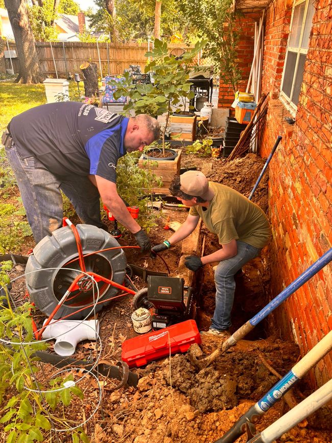 Two men are working on a drain in the backyard of a house.