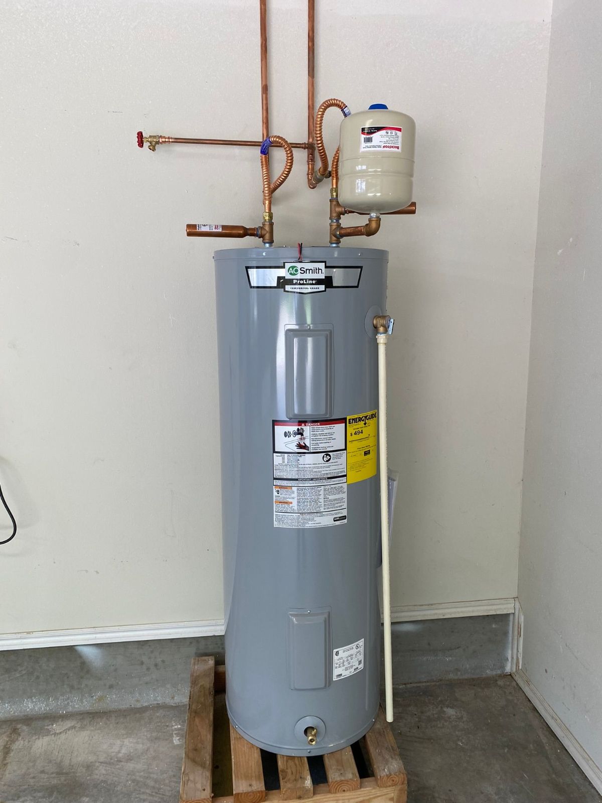A water heater is sitting on a wooden pallet in a room.