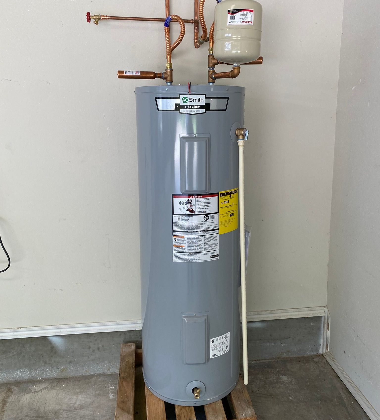 A water heater is sitting on a wooden pallet in a garage.