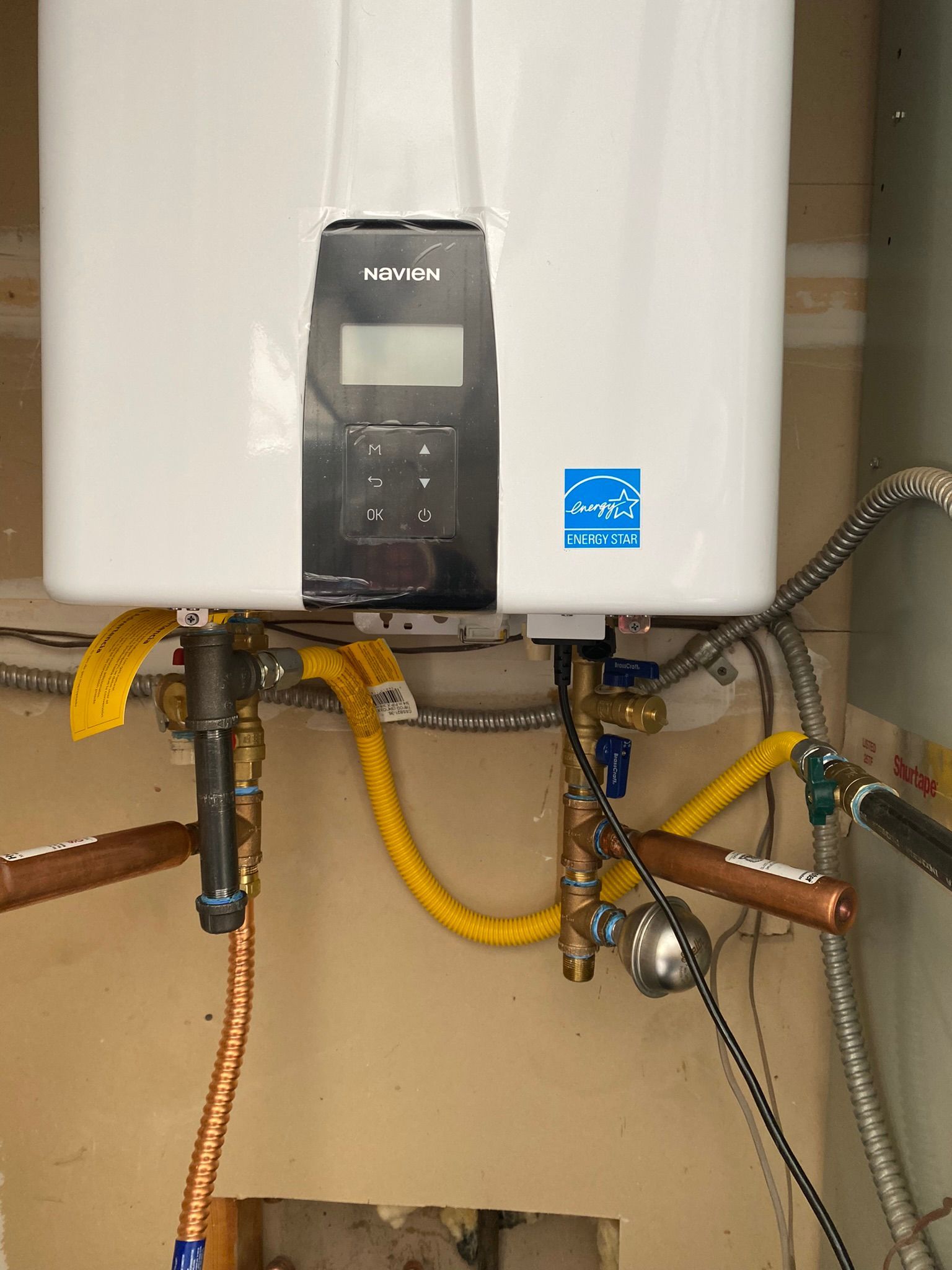 A white water heater is hanging on a wall next to copper pipes.