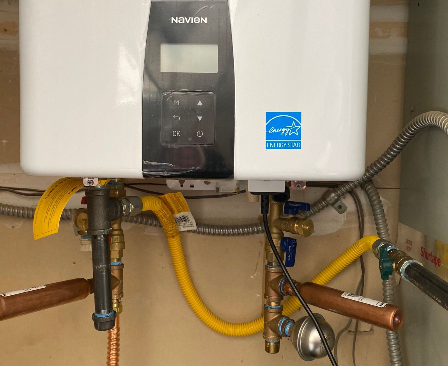 White tankless water heater with black control panel, gas and water pipes. Energy Star label.