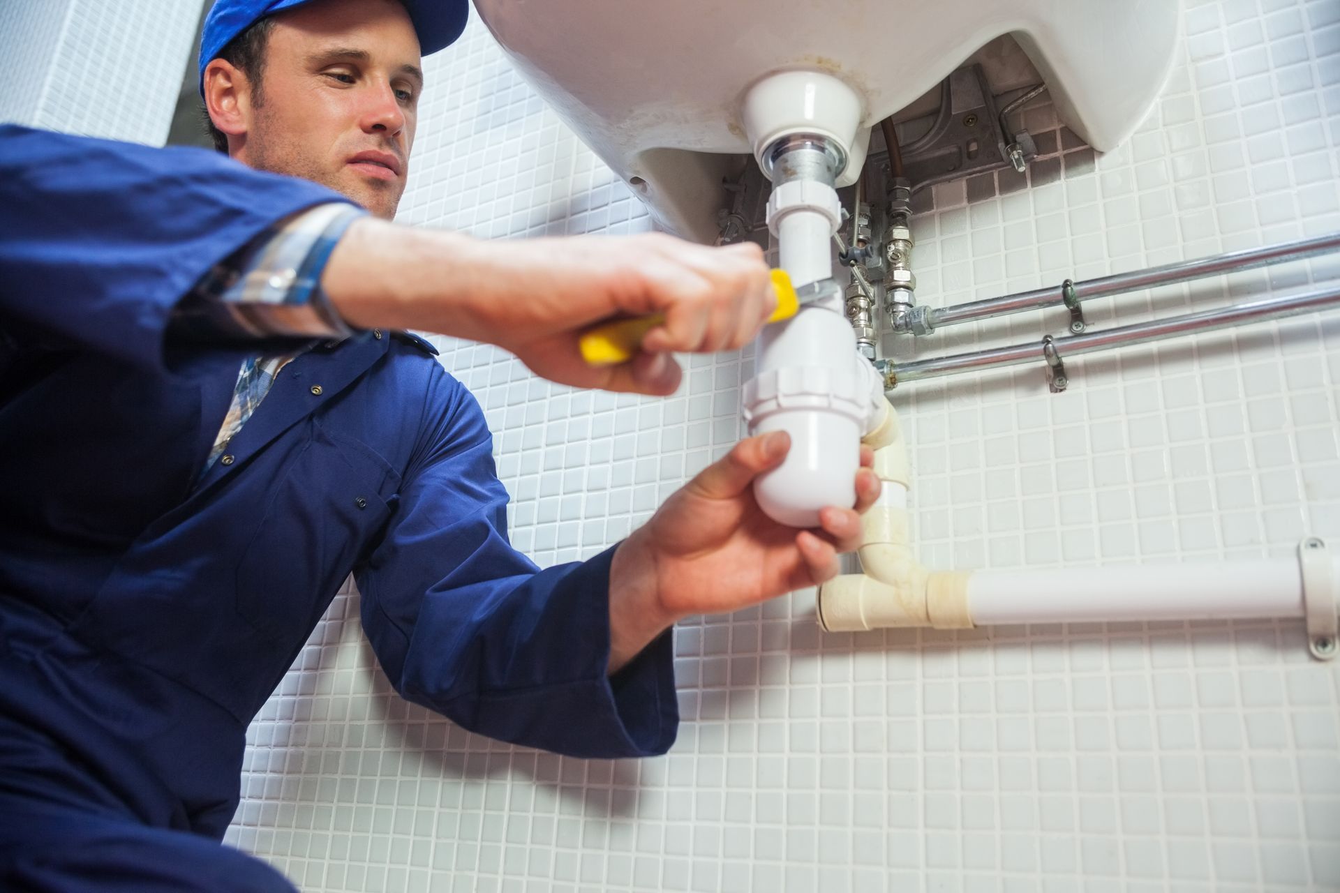 A plumber is fixing a sink with a screwdriver in a bathroom.