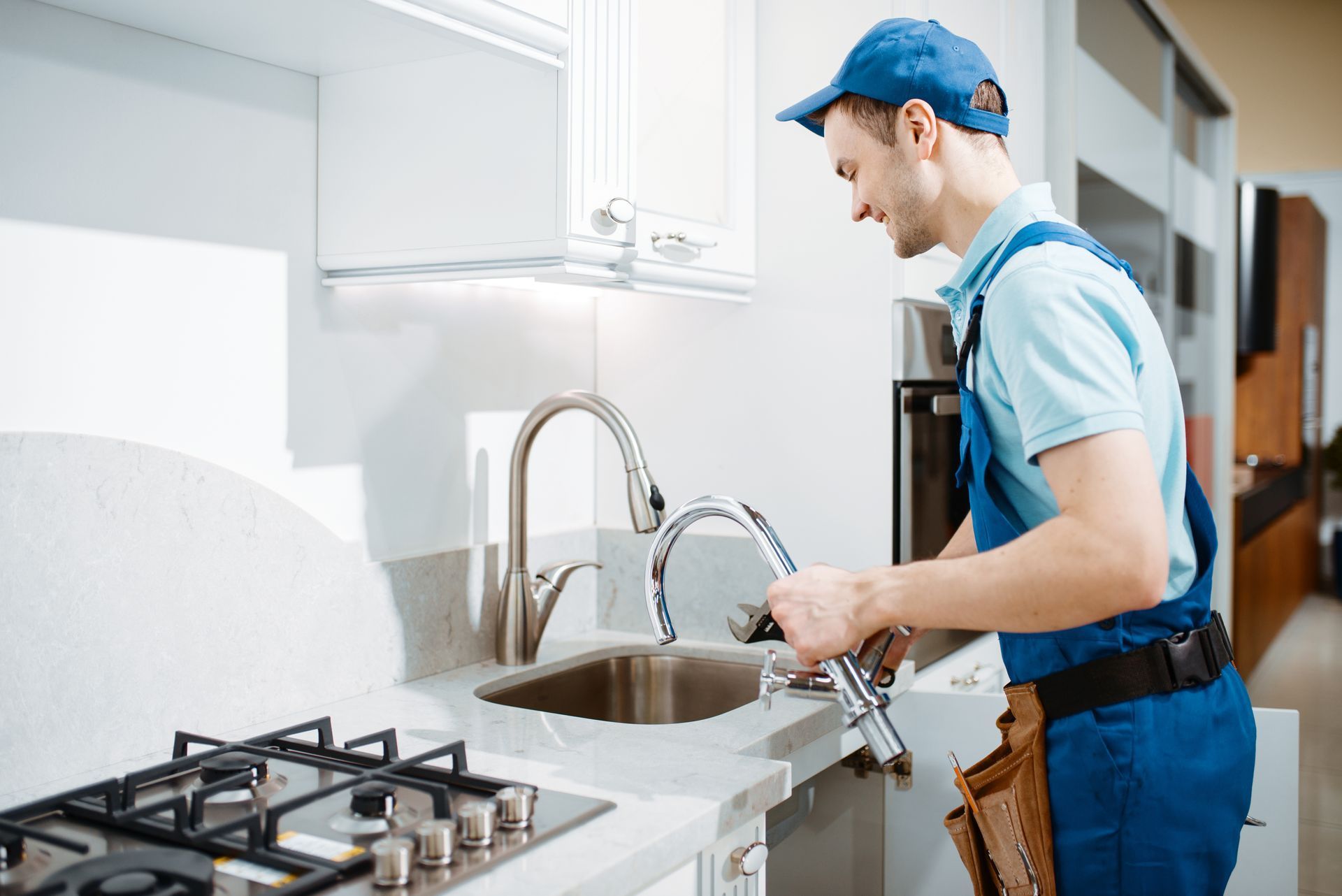 A plumber is fixing a faucet in a kitchen.