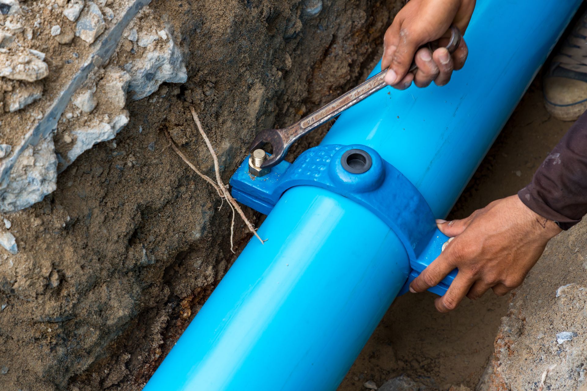 A man is fixing a blue pipe with a wrench.