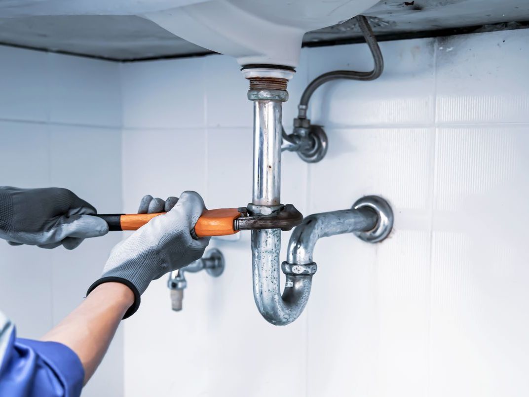 A plumber is fixing a sink pipe with a wrench.