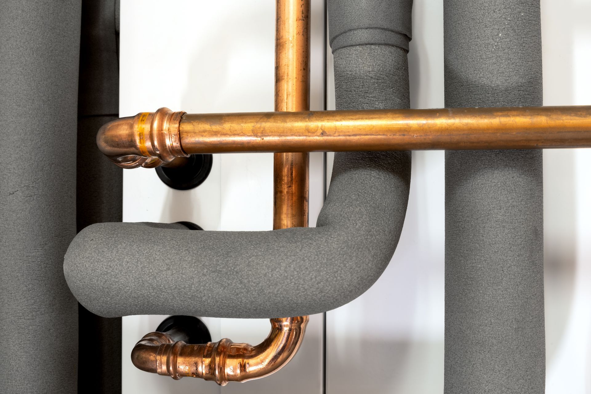 A close up of copper pipes covered in foam on a wall.