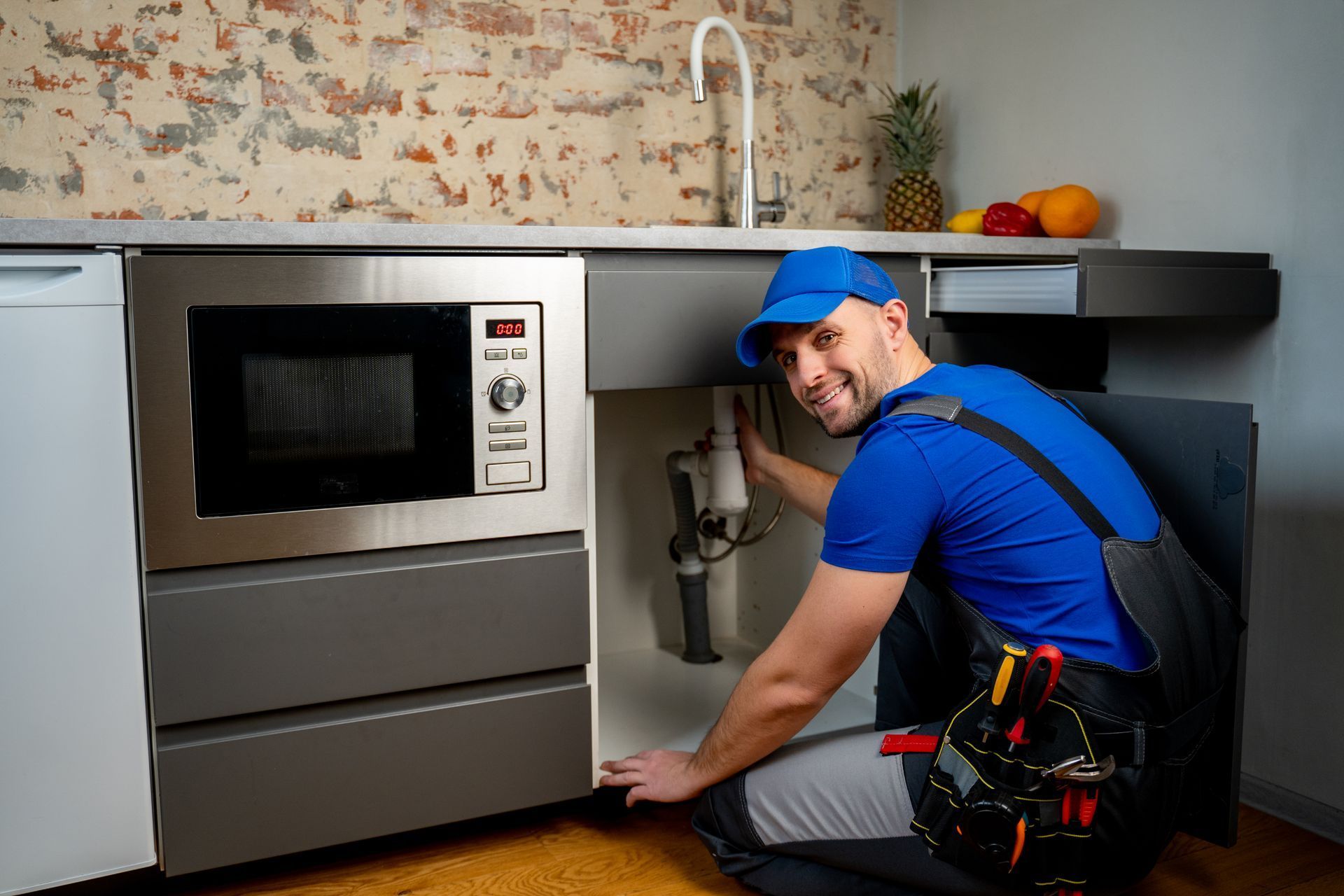 A plumber is fixing a sink in a kitchen.