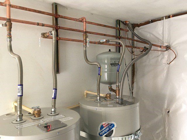 Copper pipes and water heaters in a utility room, with a pressure tank and flexible connectors.