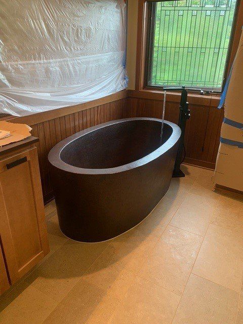 Oval, dark bathtub in a bathroom, with wood paneling, near a window and cabinetry.