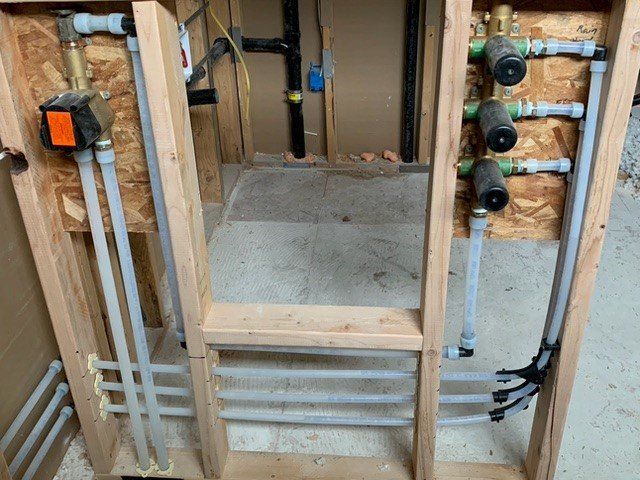 Plumbing installation within a wooden frame. PEX pipes run vertically and horizontally, with valves and fixtures in place.