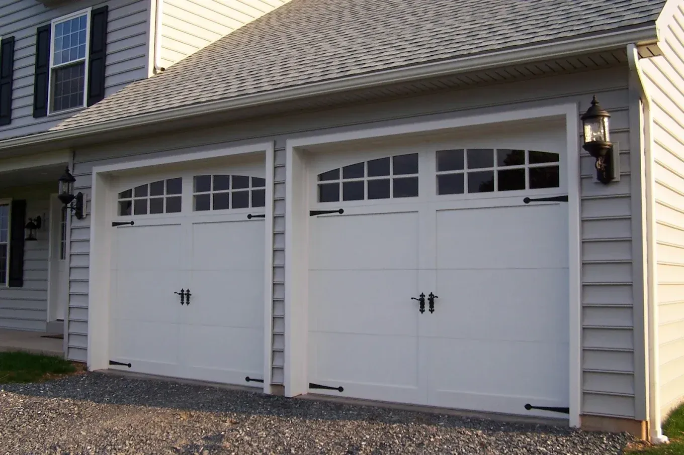 Two white garage doors with arched windows, black hardware, and sconce lighting.
