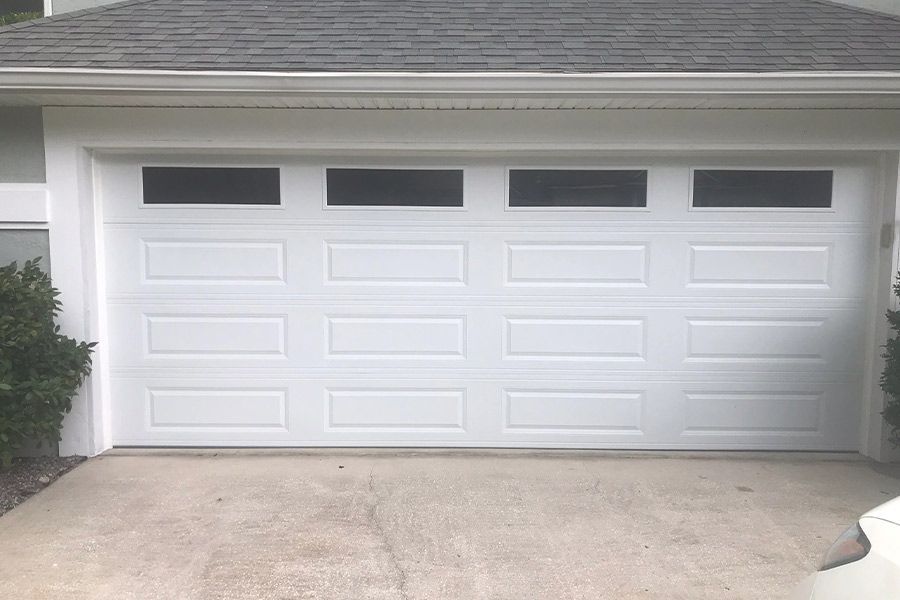 White garage door with rectangular windows above, on a concrete driveway.