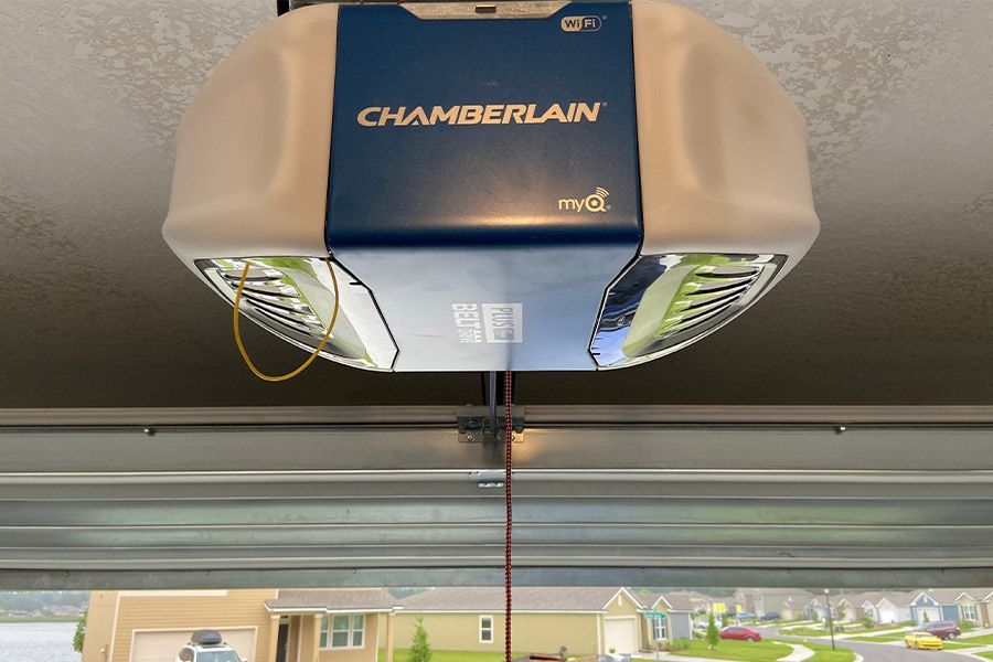 Chamberlain garage door opener unit installed in a garage, with blue and white casing. The garage door is partially open.