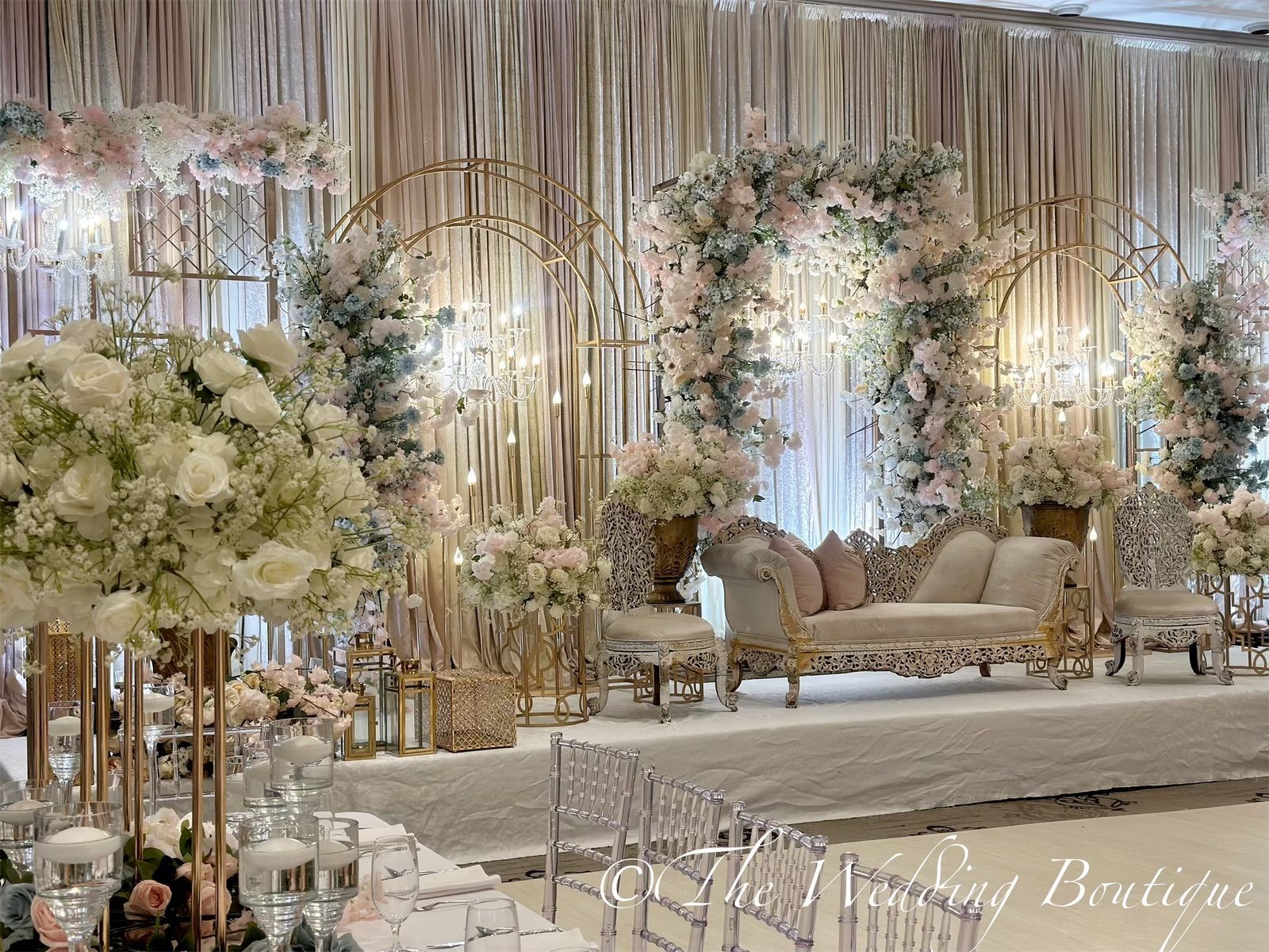 White and soft pink flowers decorating a dining table with a wedding stage and backdrop behind it