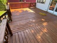 Wooden deck with brown railing and boards; attached to a white house.