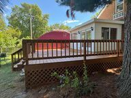 Wooden deck with railing, lattice detail, and a sunroom addition to a brick house.